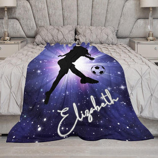 a bed covered in a purple blanket with a girl kicking a soccer ball