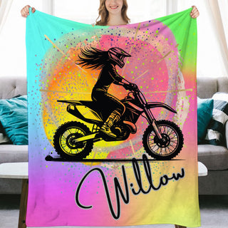 a woman holding up a colorful blanket with a picture of a girl on a dirt