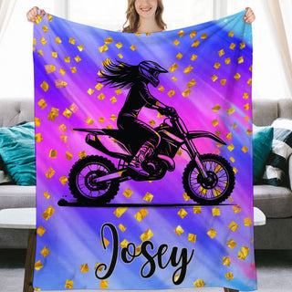 a woman holding up a purple and blue blanket with a girl on a dirt bike