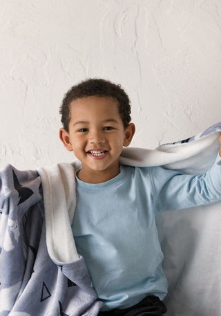 a young boy sitting on top of a bed under a blanket